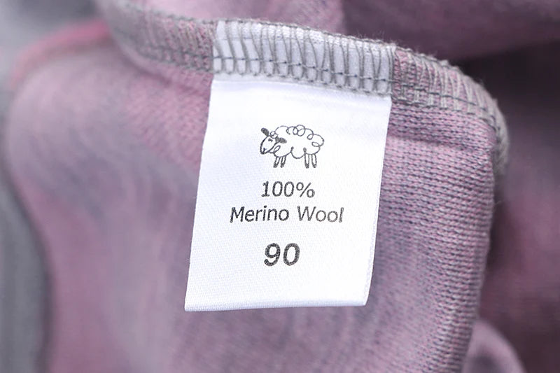 Närbild på nummerlappen på en 100% merino ull barntröja i merinoull. På nummerlappen syns storleken 90 och en handtecknad bild på en merinofår.