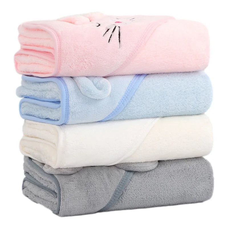 mjuka hooded handdukar i fyra olika färger vikta och balanserade fint på varandra symmetriskt. Grå längst ner, vit, blå och rosa högst upp.